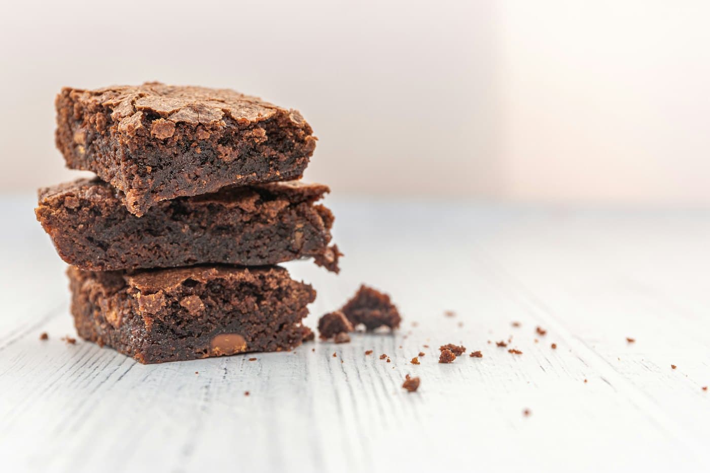 A stack of fudgy brownies with crumbs scattered on a pale table