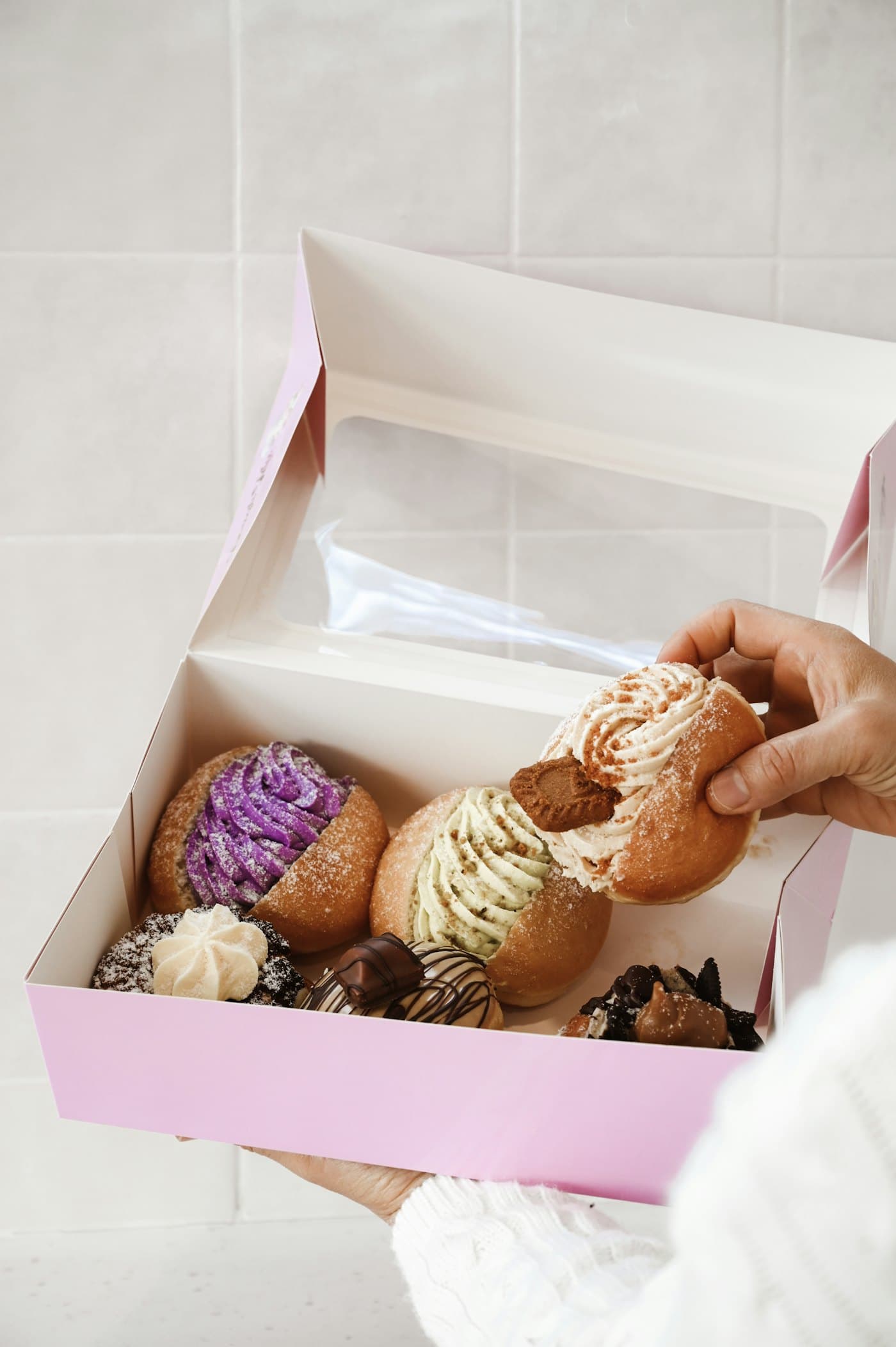 A hand reaching into a pink box of treats